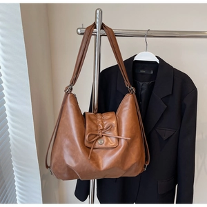 Detail of tan leather shoulder bag featuring a drawstring bow and metal buckle closure