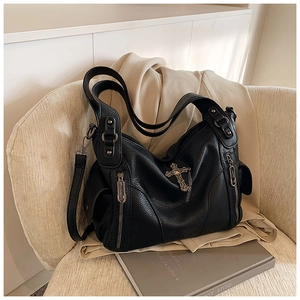 Detail of black pebbled leather tote bag with silver cross pendant and side zippers