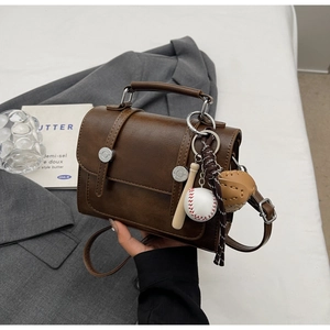 Detail of vintage coffee brown crossbody bag with silver hardware and baseball keychain