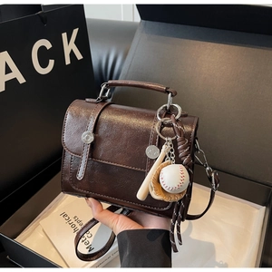 Detail of dark brown leather handbag with vintage metal buckle and baseball keychain