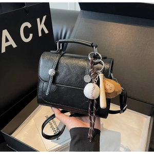 Detail of black leather satchel bag featuring a creative baseball theme charm and strap