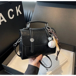 Close-up of matte black leather crossbody bag with silver buckles and baseball charm