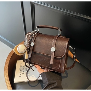 Detail of vintage brown satchel featuring leather straps and a baseball charm on a chair
