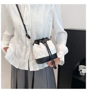 Detailed view of white quilted bucket bag with black base and elegant gold hardware