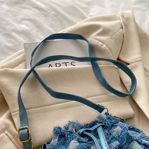 Detail of blue denim shoulder bag with frayed edges and adjustable leather strap