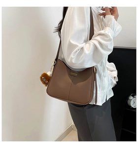 Détail d'un sac seau en cuir marron mat avec breloque ours en peluche et lettrage fashion