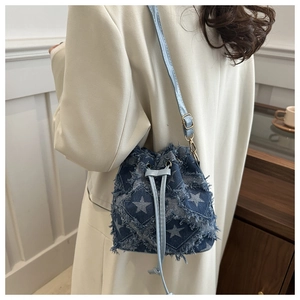 Détail du sac seau en denim bleu avec motif étoile et bords effilochés porté par un mannequin