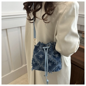 Detail of blue denim bucket bag with star patterns and frayed edges on a model