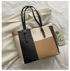Detail of color-block tote bag showing PU leather texture and size comparison with phone