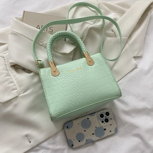 Detail of mint green crocodile-textured handbag with woven handle and gold accents