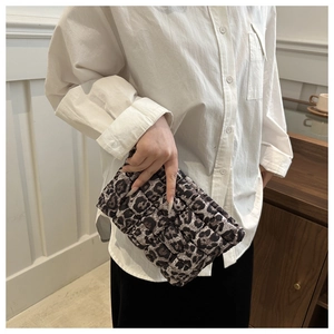 Close-up of leopard print quilted clutch bag held by hand in a chic cafe setting