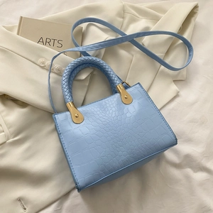 Detail of light blue crocodile-embossed leather handbag with woven handle and gold hardware