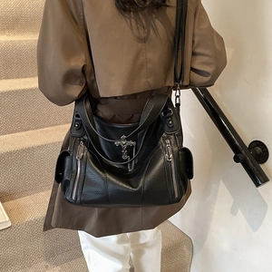 Black pebbled leather tote bag for women with silver cross charm on a staircase
