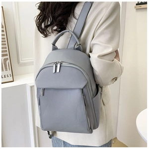 Side view of woman wearing a grey-blue lychee texture leather backpack in a home setting