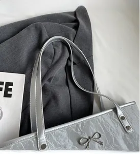 Détail du sac cabas argenté avec nœud décoratif et poignée renforcée par rivets