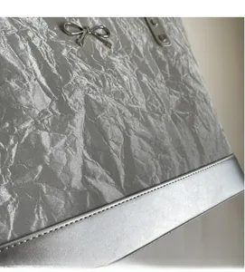 Détail du sac seau argenté montrant le tissu froissé texturé et le nœud métallique