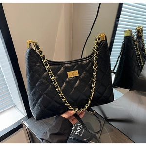 Detail of black quilted hobo bag featuring a gold chain strap and a metallic turn-lock