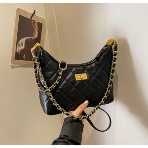 Detail of black quilted leather crescent bag with bold gold chain held by hand