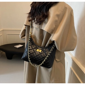 Quilted black leather tote bag with gold chain strap worn over a beige trench coat