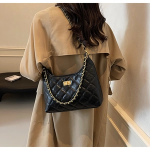 Quilted black hobo bag with gold chain strap worn over a khaki trench coat