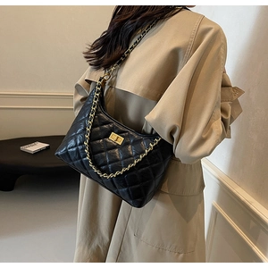Detail of black quilted leather shoulder bag with gold chain strap on a trench coat