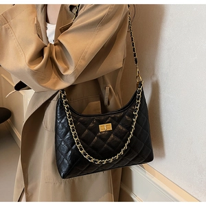 Close-up of quilted black leather tote bag with gold chain strap on a khaki trench coat