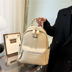 Beige faux leather women's backpack with pebble texture and silver zippers on desk