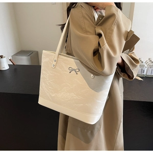 Détail du sac cabas plissé crème avec nœud métallique porté avec un trench-coat