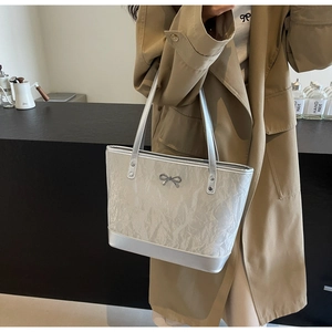 Détail du sac cabas argenté métallisé avec texture plissée et breloque nœud sur l'épaule