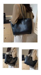 Detailed view of the black leather tote bag with a golden metal nameplate and double straps