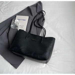 Flat lay of black leather tote bag with FASHION & BAGS logo and shoulder straps