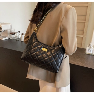 Close-up of black quilted leather shoulder bag with gold chain strap and metal lock