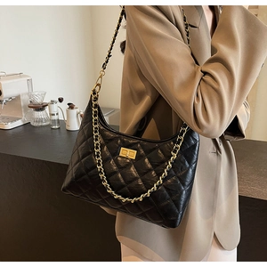 Detail of a black quilted leather chain tote with a golden clasp on a model shoulder