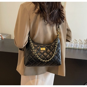 Close-up of black quilted hobo bag with gold chain and turn-lock on a brown suit jacket