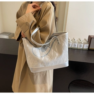 Détail du sac cabas argenté avec texture plissée et accent de nœud métallique à l'épaule