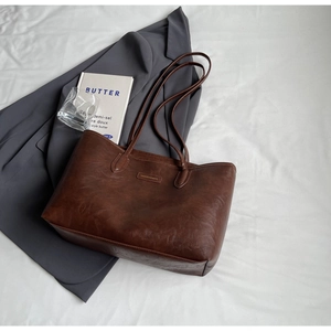 Close-up of brown textured leather tote bag featuring an embossed brand logo tag on the front