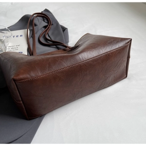 Detailed view of the wide base and pleated vintage leather texture of this brown tote bag