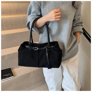 Detail of black matte tote bag with thin buckle strap held by model on stone stairs