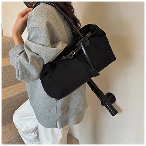 Detail of a black matte tote bag with slim leather straps and metal buckles on a model