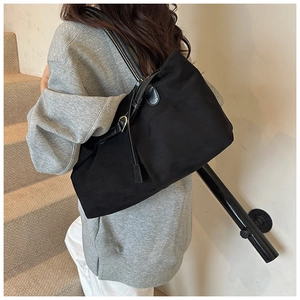 Detail view of a large black matte tote bag with leather straps and metal buckle