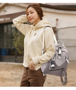 Close-up of light grey casual backpack with white straps and cute bear pendant decor