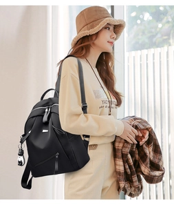 Detail of black nylon backpack with silver zippers and a cute teddy bear charm