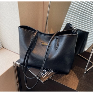 Close-up of textured black leather tote bag with gold metal fashion logo and handles