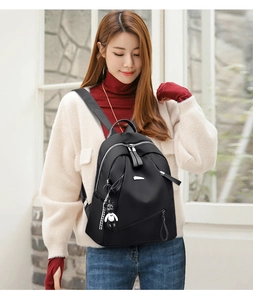 Detailed side view of black nylon backpack with a cute bear charm on a female model