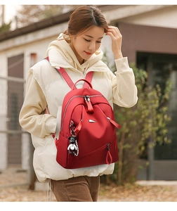 Detail of dark red waterproof backpack with silver zippers and cute bear charm