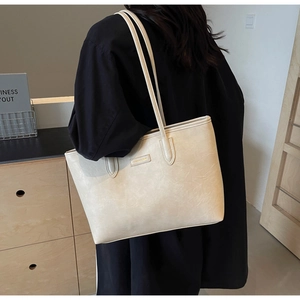 Detail of a beige tote bag with soft faux leather texture and gold logo plate