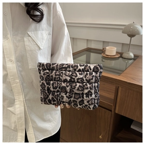 Detail of leopard print quilted clutch bag held by hand in a cozy indoor setting