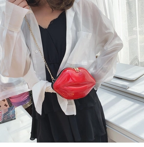 Close-up of a red lip-shaped crossbody bag with glossy patent finish and gold chain strap