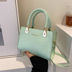Detail of mint green crocodile pattern bag with woven handles and fashion lettering