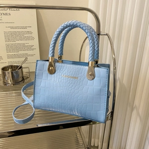 Detail of light blue crocodile embossed handbag with woven handles and golden hardware